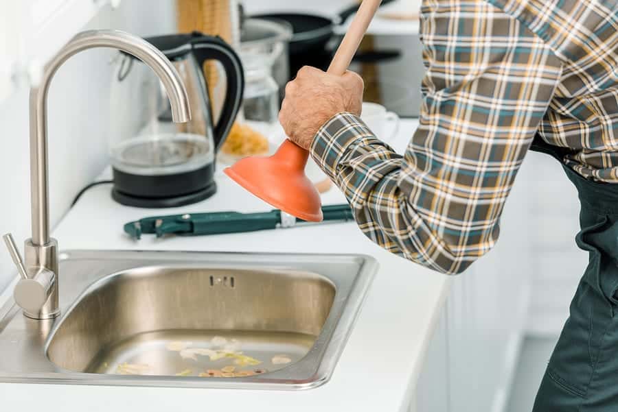 Plumber Using Plunge And Cleaning Sink In Kitc